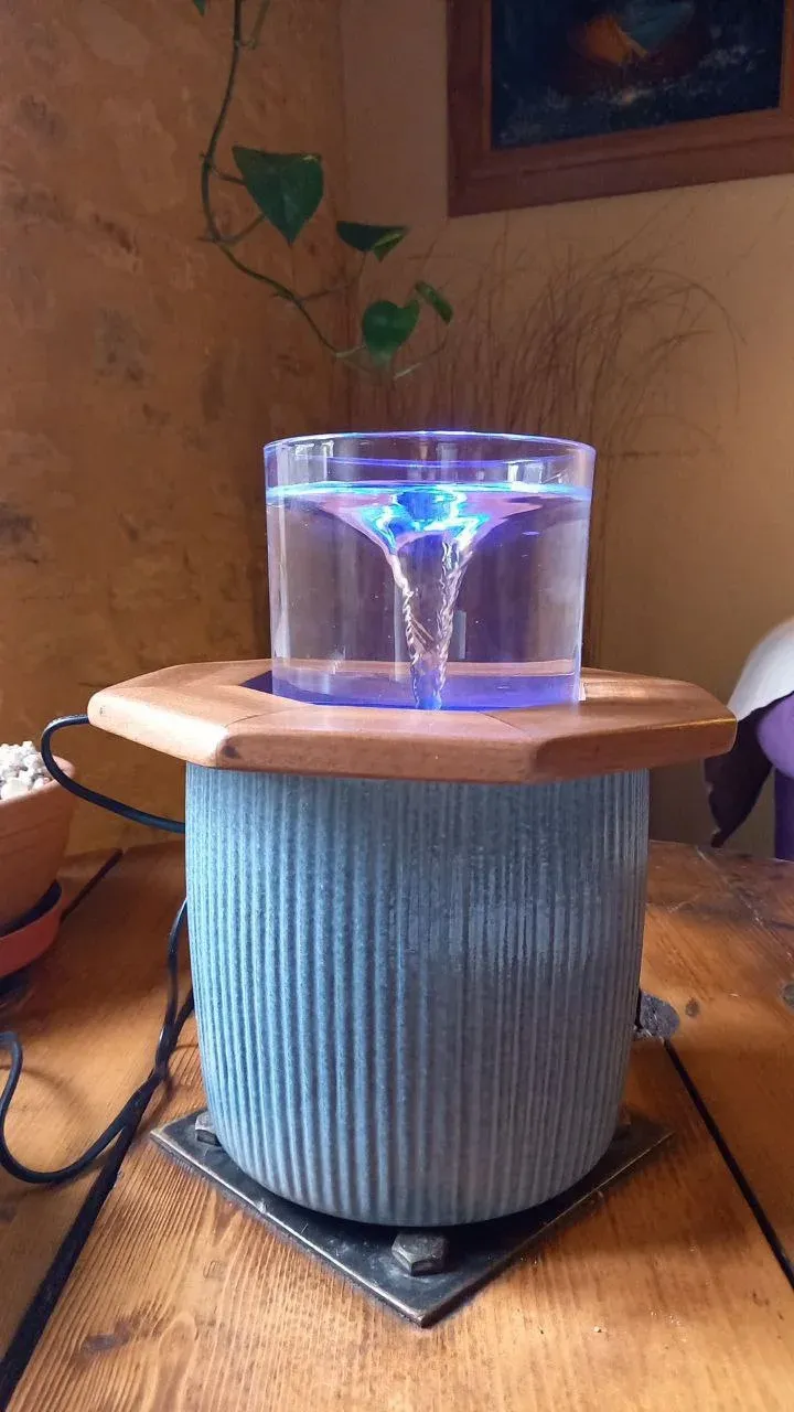 Une fontaine allumée en violet, posée sur un pot gris, dans une pièce